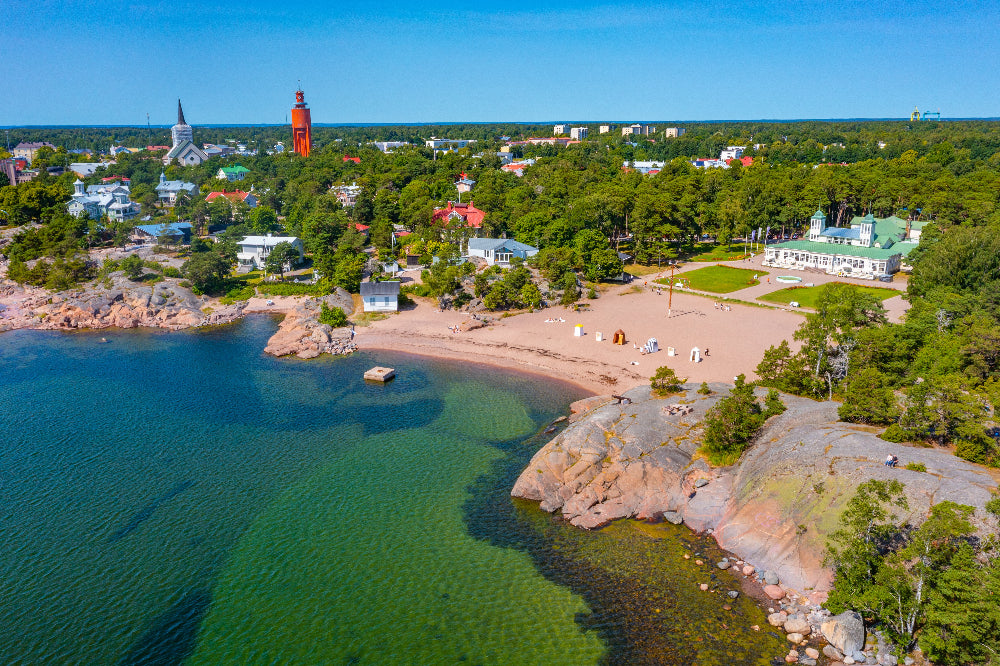 Aerial view of a coastal town Hanko (Finland) with villas, green trees, blue water, and beaches.