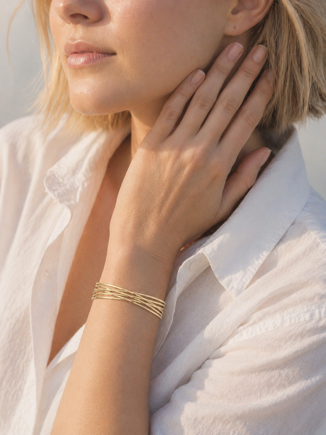 Gold-tone layered cuff bracelet with flowing sculptural lines worn on the wrist by HNKO