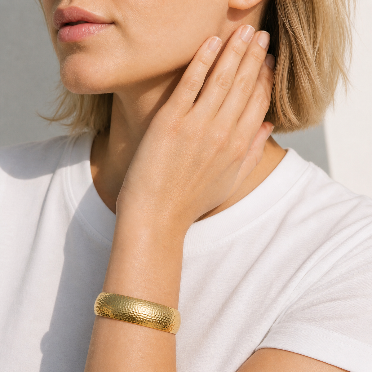 Gold-tone hammered cuff bracelet with a textured sculptural finish worn on the wrist by HNKO