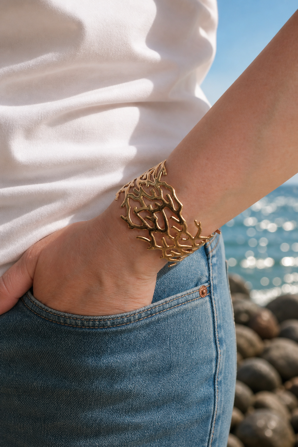 Person wearing a gold coral bracelet cuff by the sea
