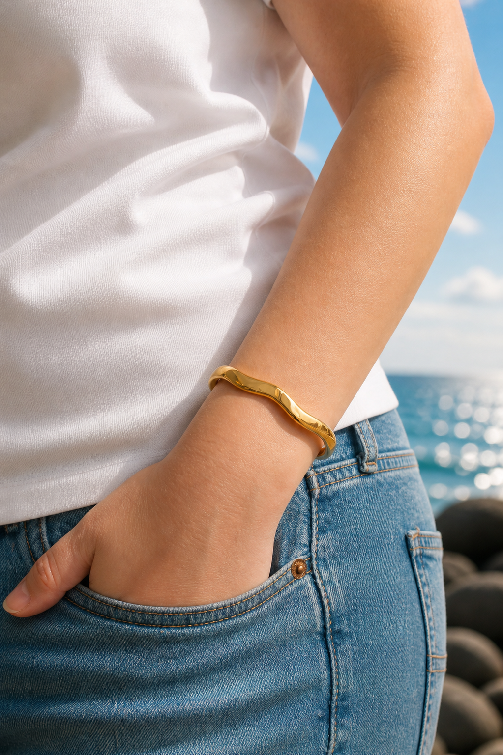 Person wearing a gold waved bracelet with a scenic background of water and sky