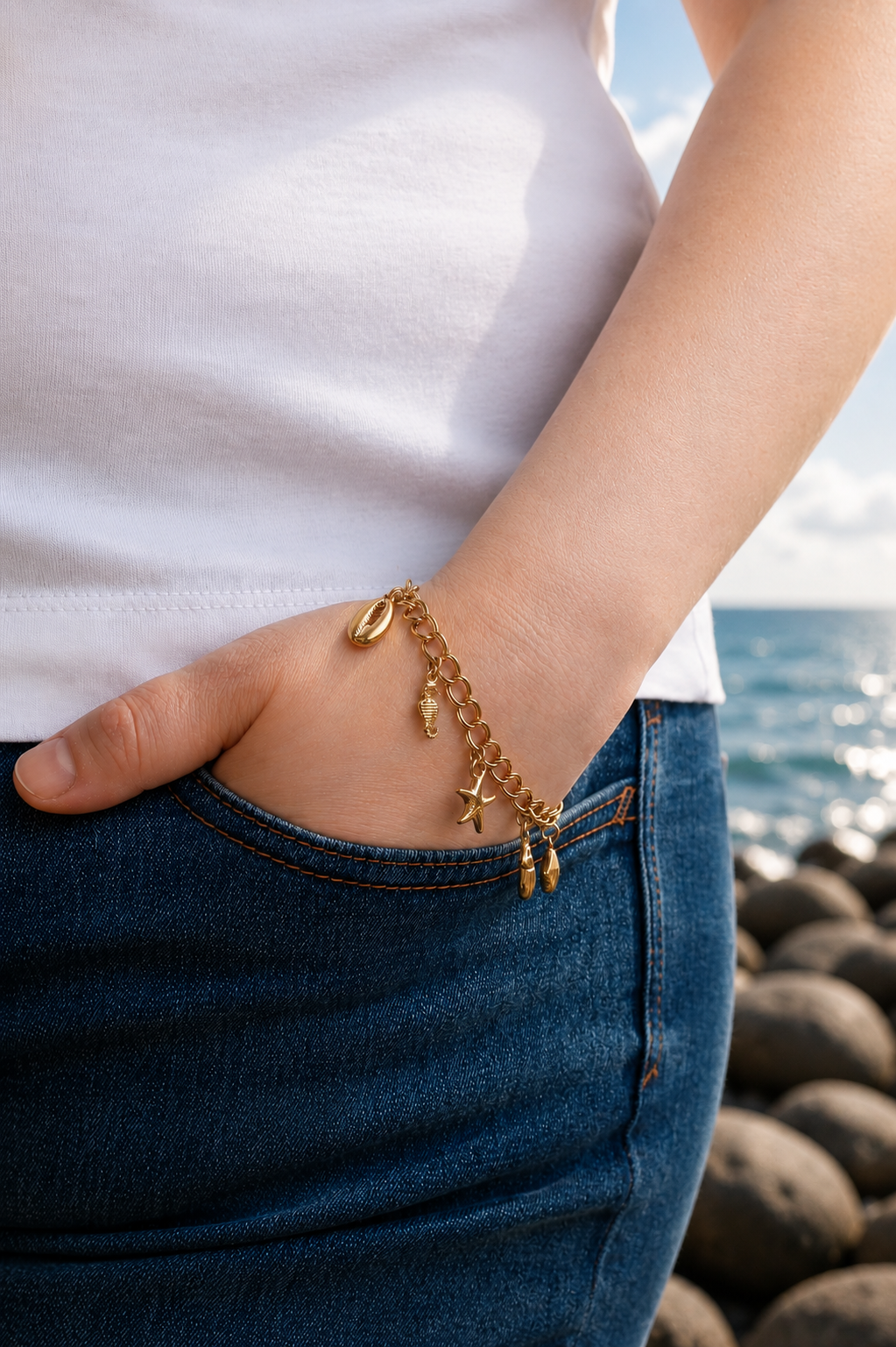 Model wearing a gold charm bracelet with seashell and starfish pendants by HNKO Finland