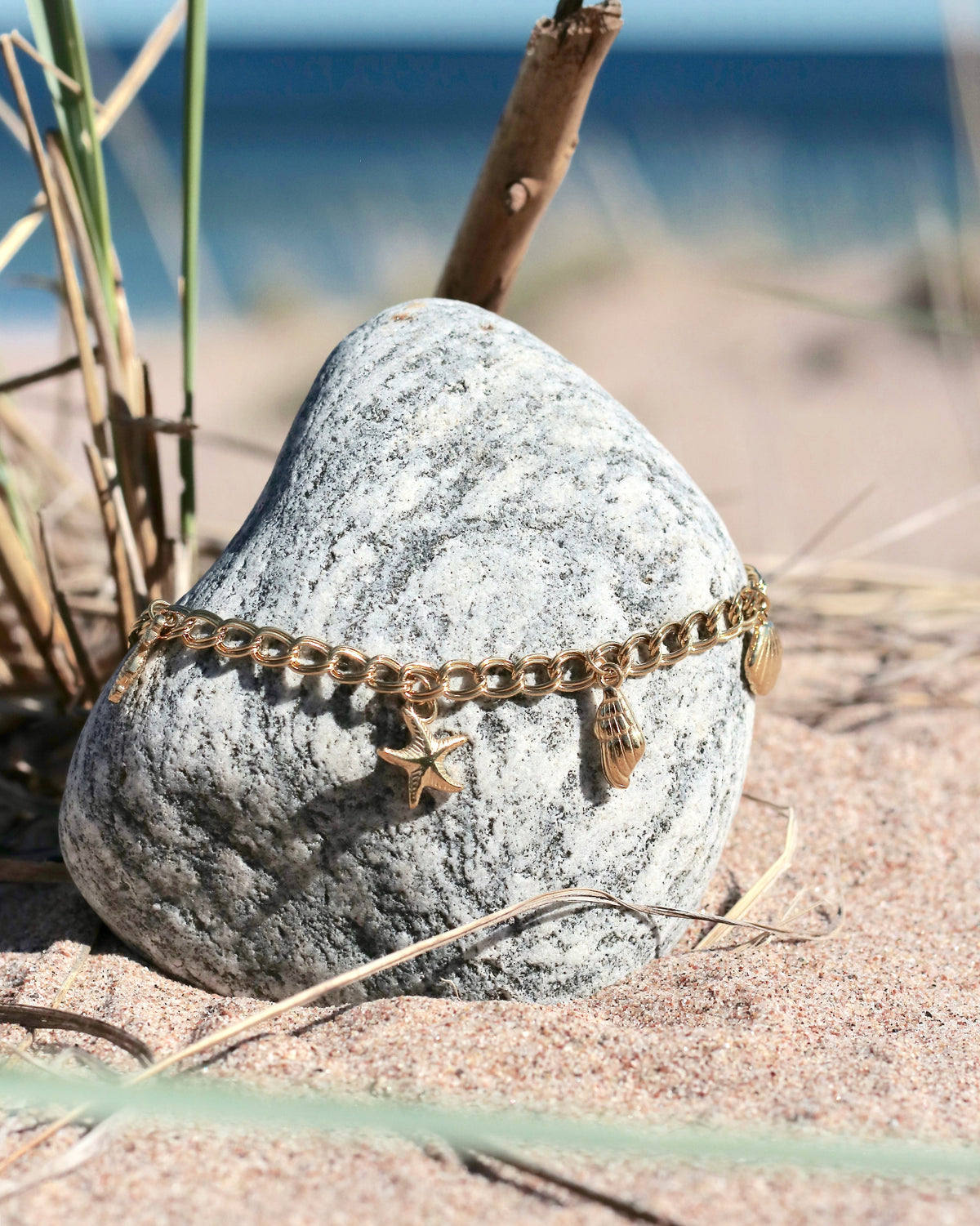Gold-tone charm chain necklace with starfish, shell and seahorse charms displayed on a beach stone in Hanko, Finland