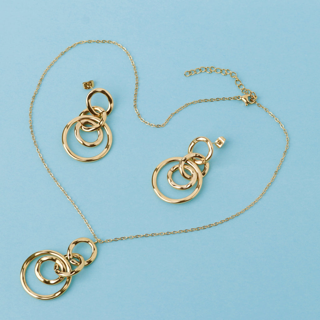 Gold jewelry set featuring a necklace and matching earrings with interlocking circular ring pendants, displayed on a light blue background.