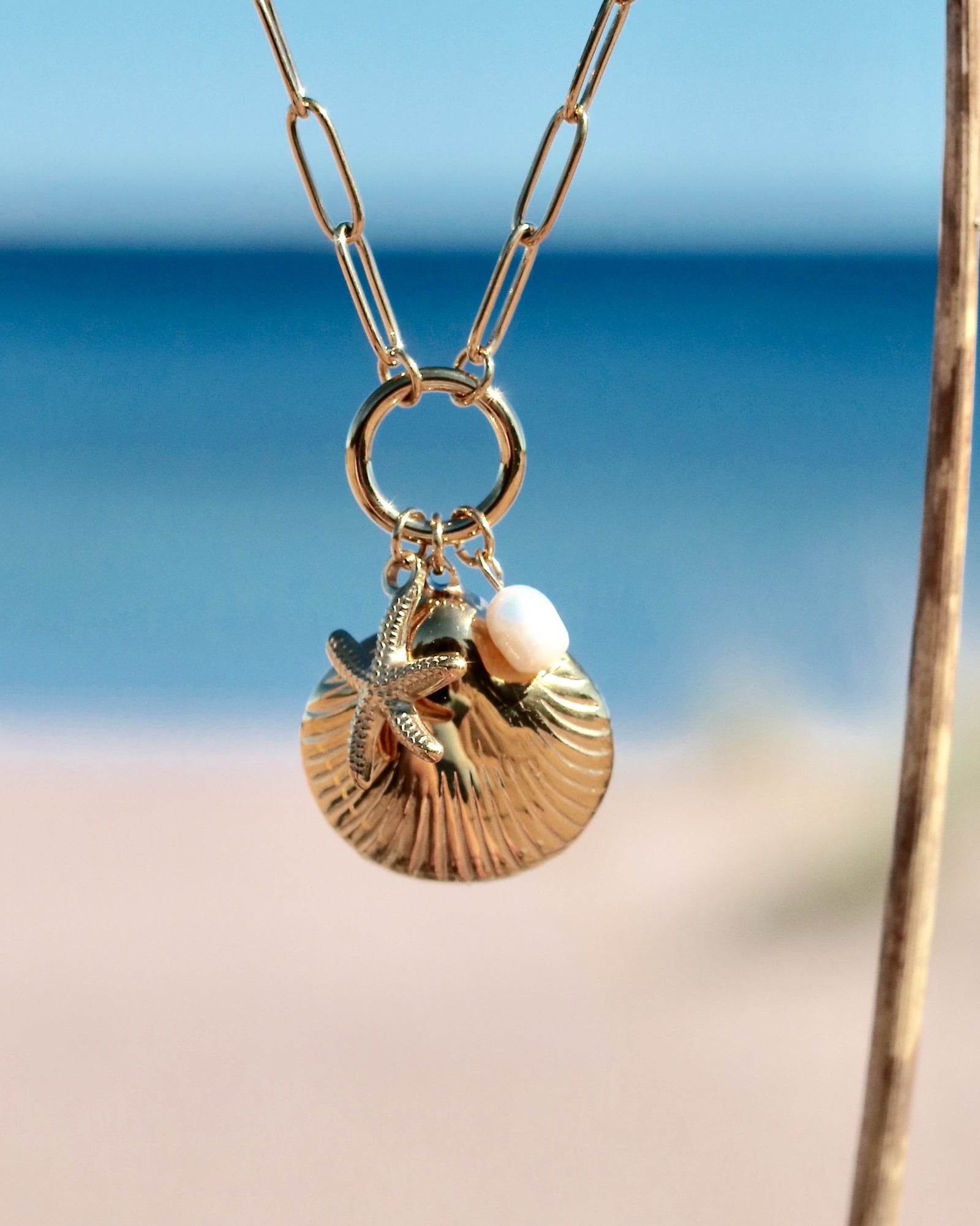 Gold-tone charm necklace with a seashell pendant, starfish charm and freshwater pearl photographed by the sea in Hanko, Finland