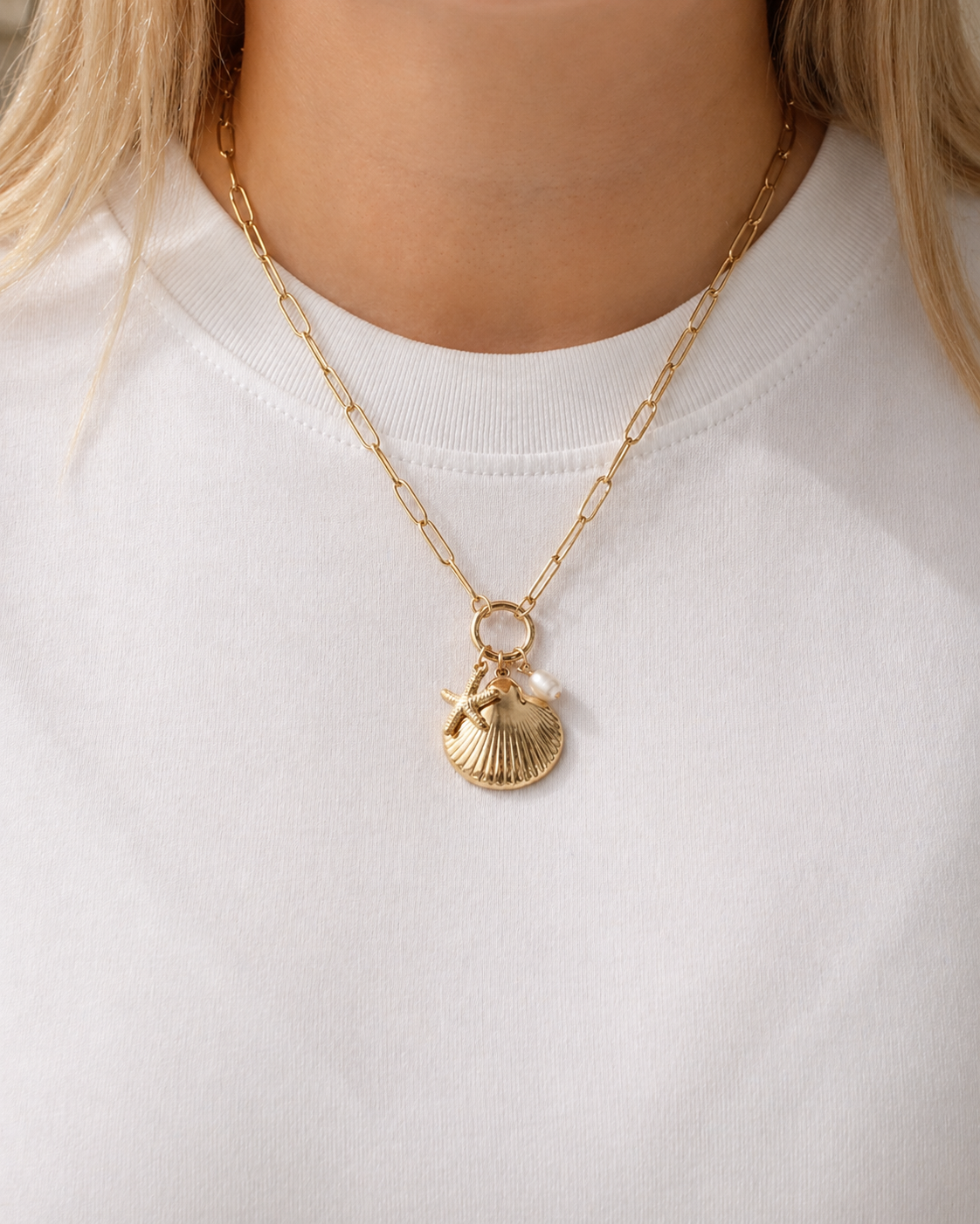 Gold-tone charm necklace with a seashell pendant, starfish charm and freshwater pearl worn by a model by HNKO
