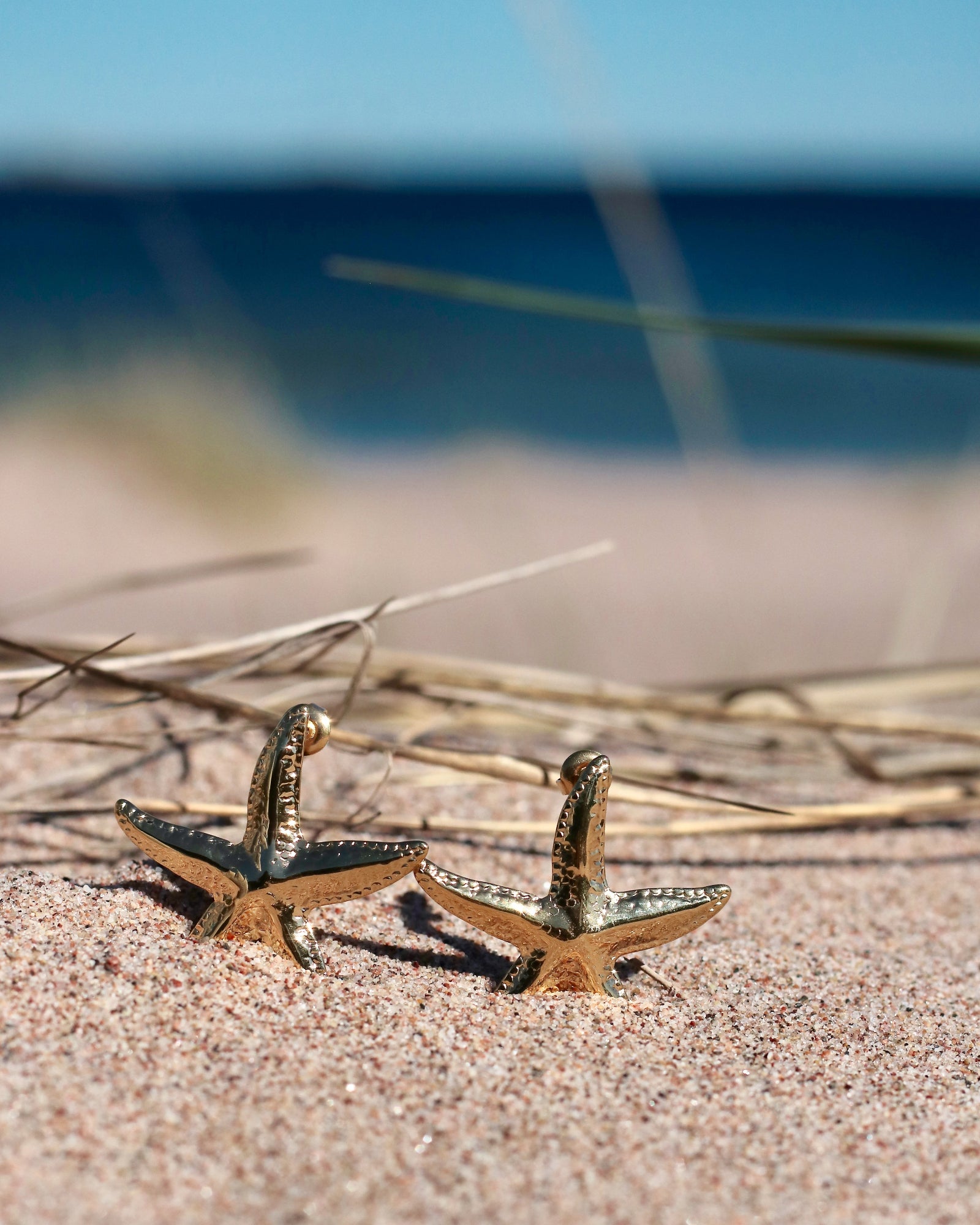 Gold-tone starfish stud earrings displayed on beach sand in Hanko, Finland