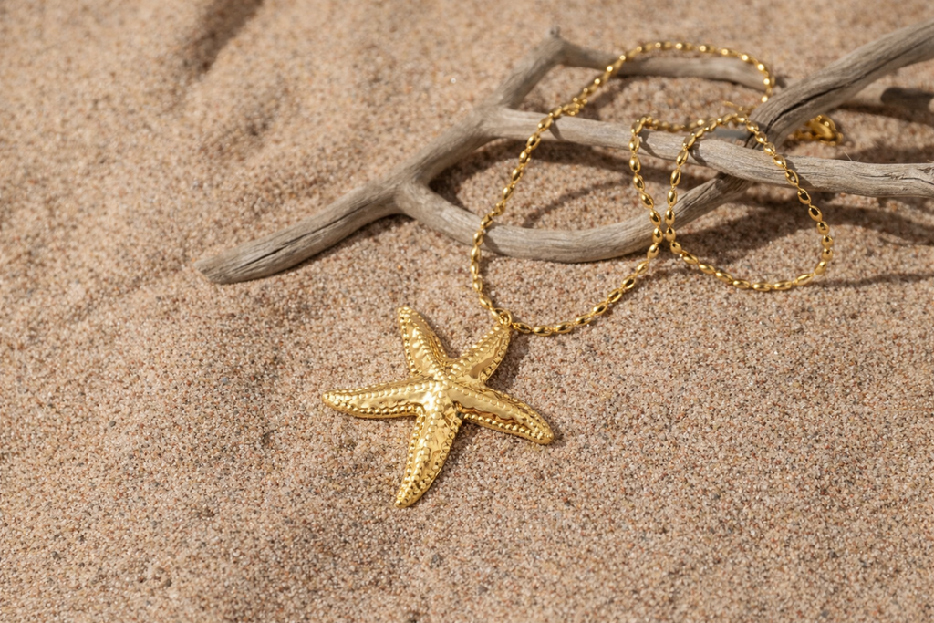 Gold-tone starfish pendant necklace displayed on beach sand, inspired by Nordic coastal life in Hanko, Finland by HNKO