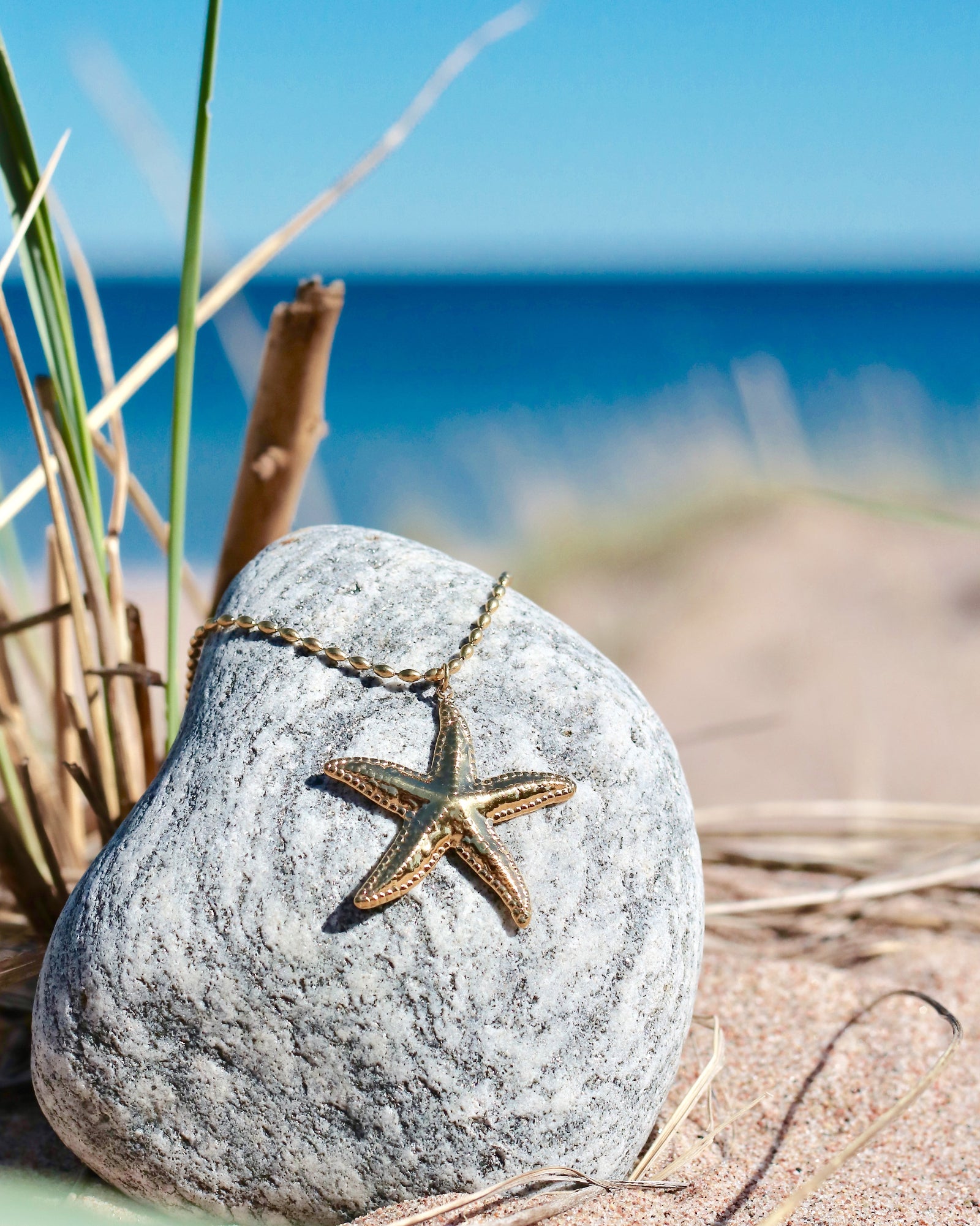 Gold-tone starfish pendant necklace displayed on a beach stone with the sea in the background in Hanko, Finland
