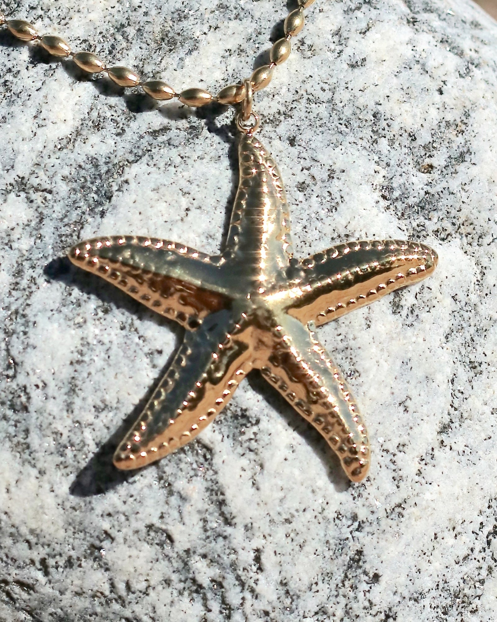Close-up of a gold-tone starfish pendant necklace photographed on a coastal stone in Hanko, Finland